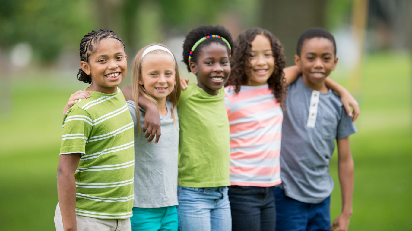 Five childrent of diverse ethnicities standing together with hands over each other's shoulders looking at the camera smiling